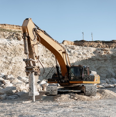 Excavator breaking apart rocks in a quarry under a bright blue sky, showcasing the power of heavy machinery in construction and mining